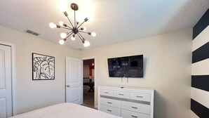 Une chambre à coucher comprenant un lit, une commode, un téléviseur et un luminaire fixé au plafond.