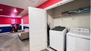 Une buanderie avec un lave-linge et un sèche-linge blancs, un canapé beige et un mur rouge et bleu.