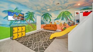 Une pièce décorée d’une fresque représentant une plage, avec un canapé, un toboggan jaune et un meuble.