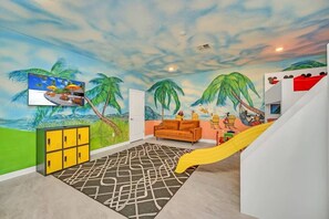 A room with a beach mural, a sofa, a yellow slide, and a cabinet.