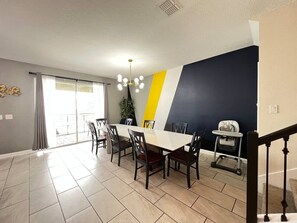 A dining area with a table and chairs, a staircase, and a view through a glass door.