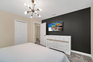 A bedroom with a bed, a dresser, a television on the wall, and a ceiling light fixture.