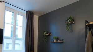 A modern living room with a sofa, a window with curtains, and wall-mounted shelves with plants. - Renovated studio 5 minutes from the city center (Rouen)