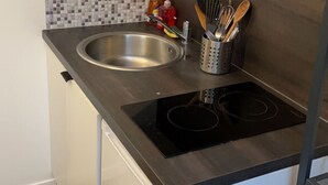 A compact kitchen with a stainless steel sink, a black induction cooktop, and a tiled backsplash. - Renovated studio 5 minutes from the city center (Rouen)