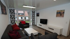 Een moderne woonkamer met een bank, fauteuils, een salontafel en een televisie op een witte dressoir.