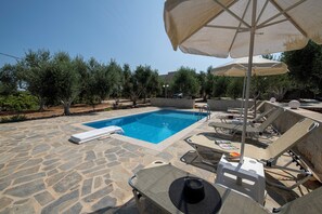 A stone pool with lounge chairs and umbrellas, surrounded by trees. - Villa Amelia, modern and tasteful house in Cretan nature (Rethymno)