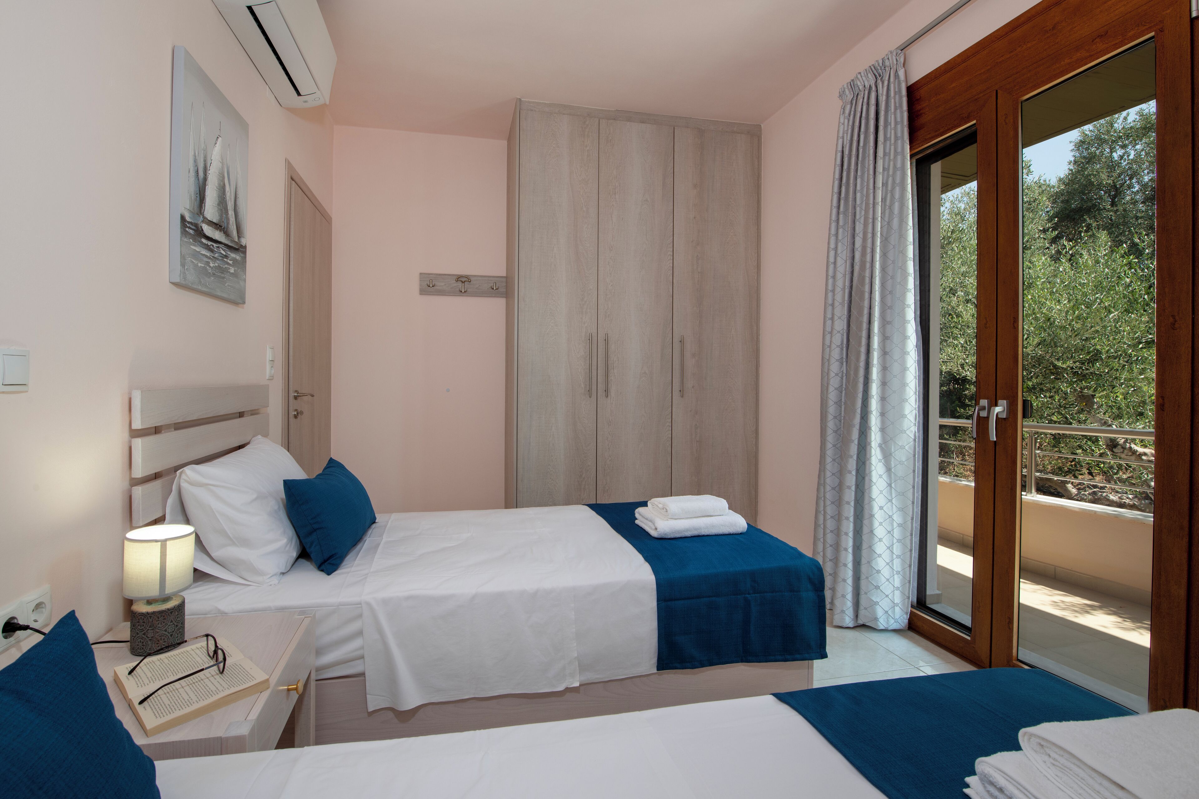 Habitación de hotel con dos camas, una mesita de noche, una lámpara y vistas al exterior.