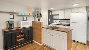 A kitchen with white cabinets, a wooden countertop, a microwave, and a coffee maker.