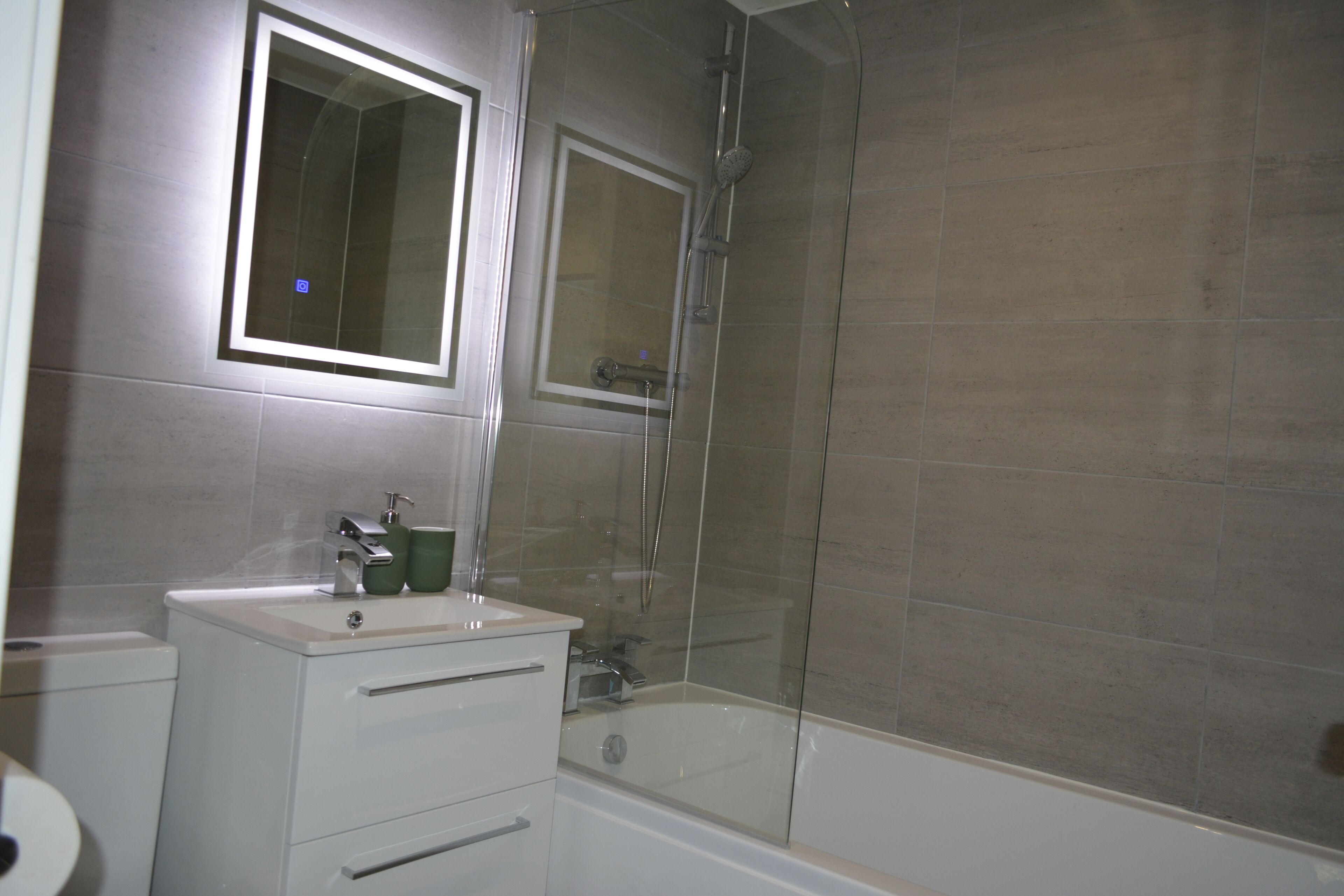 Een badkamer met een bad, een douche met glazen wanden, een wastafel met spiegel erboven en een toilet.