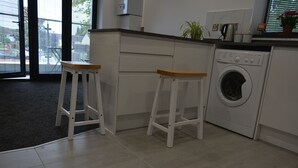 Una cocina con lavadora, dos taburetes y una ventana con persianas.
