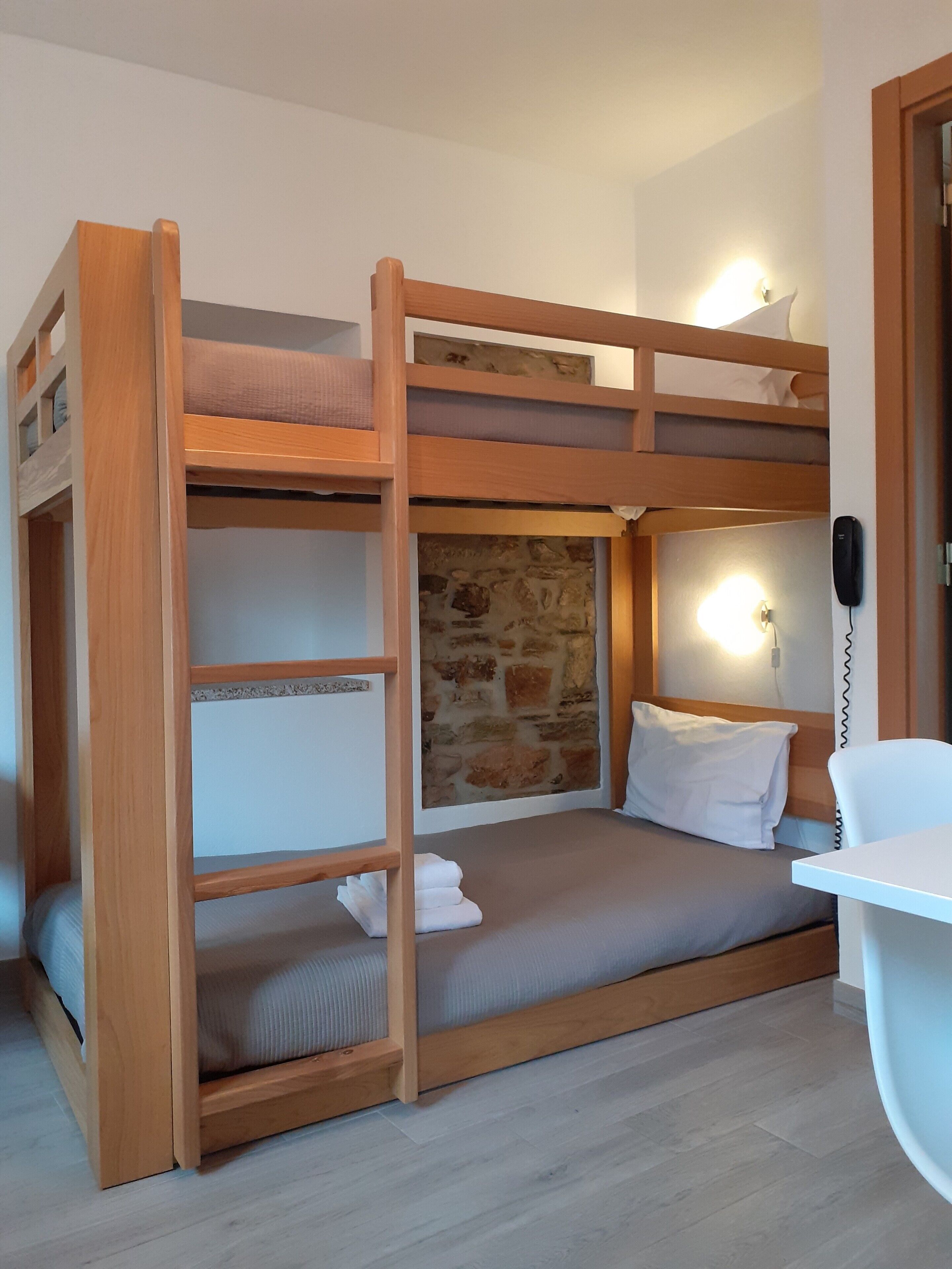 A bunk bed with a desk and a stone wall.