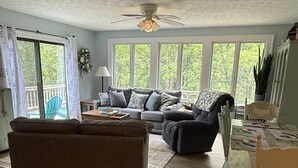 A spacious living room with a large sofa, a smaller sofa, and a dining table with chairs. There is a ceiling fan, a window with a view of trees, and a sliding glass door leading to an outdoor area. - gaze at Seneca Rocks from living room sofa (Seneca Rocks)