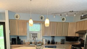 A kitchen with wooden cabinets, a central island with stools, a stove, and a refrigerator. - gaze at Seneca Rocks from living room sofa (Seneca Rocks)