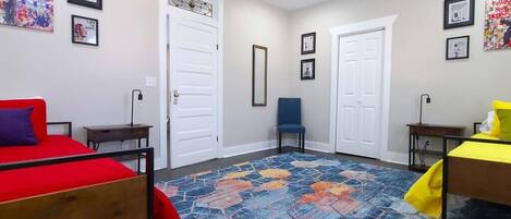 Quarto com duas camas, um tapete colorido e quadros nas paredes.