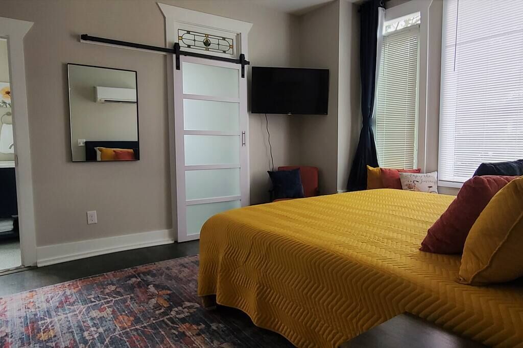 Een slaapkamer met een bed, een televisie, een schuifdeur en een raam met gordijnen.