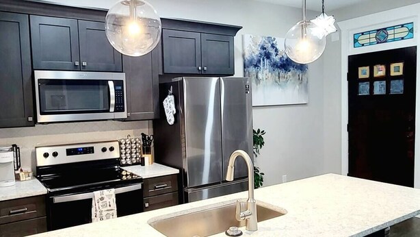 A modern kitchen with dark cabinets, stainless steel appliances, a white countertop, and pendant lighting. - West End Jewel on Sunset (Winston-Salem)