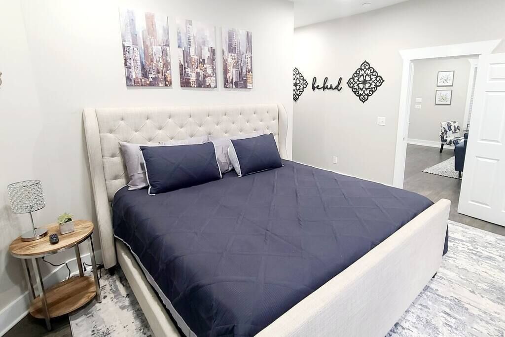 A bedroom with a large bed, a round side table, and a cityscape artwork on the wall.