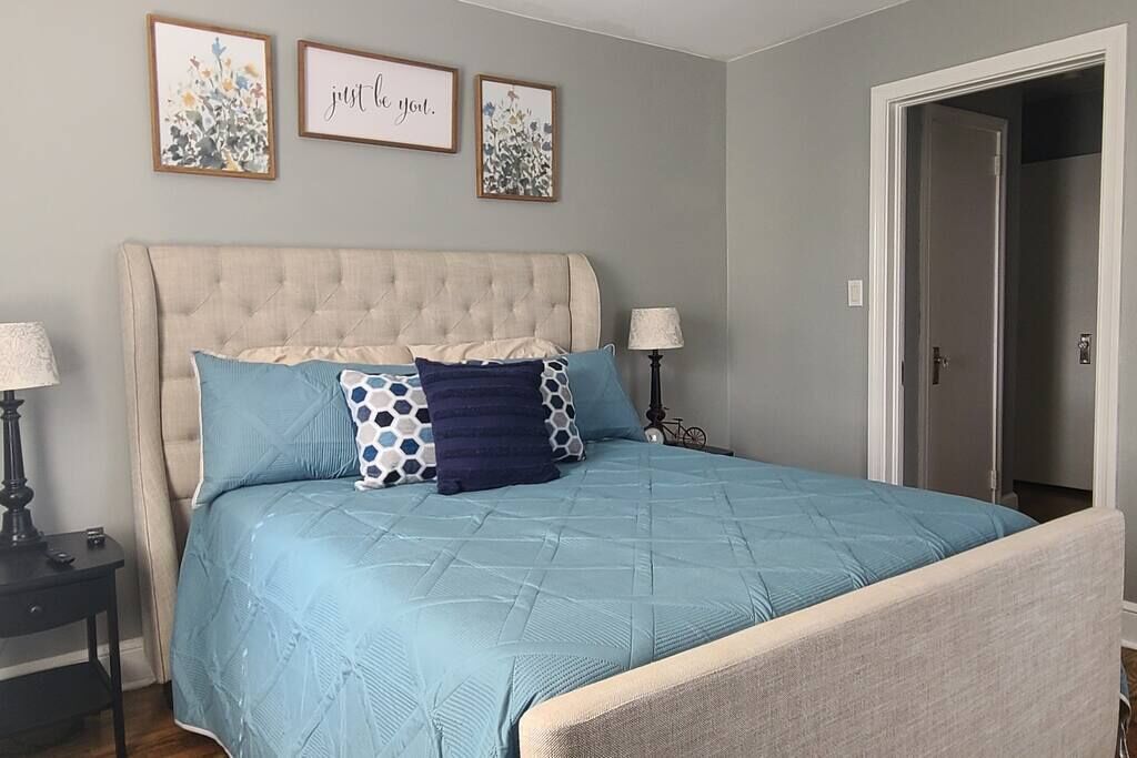 Un dormitorio con un cabecero capitonado, una colcha azul acolchada y tres cuadros con motivos florales en la pared.