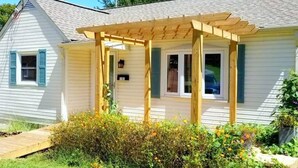 A house with a covered porch, a small garden with flowers, and a wooden deck. - Cozy Ardmore Cottage Main Level (Winston-Salem)