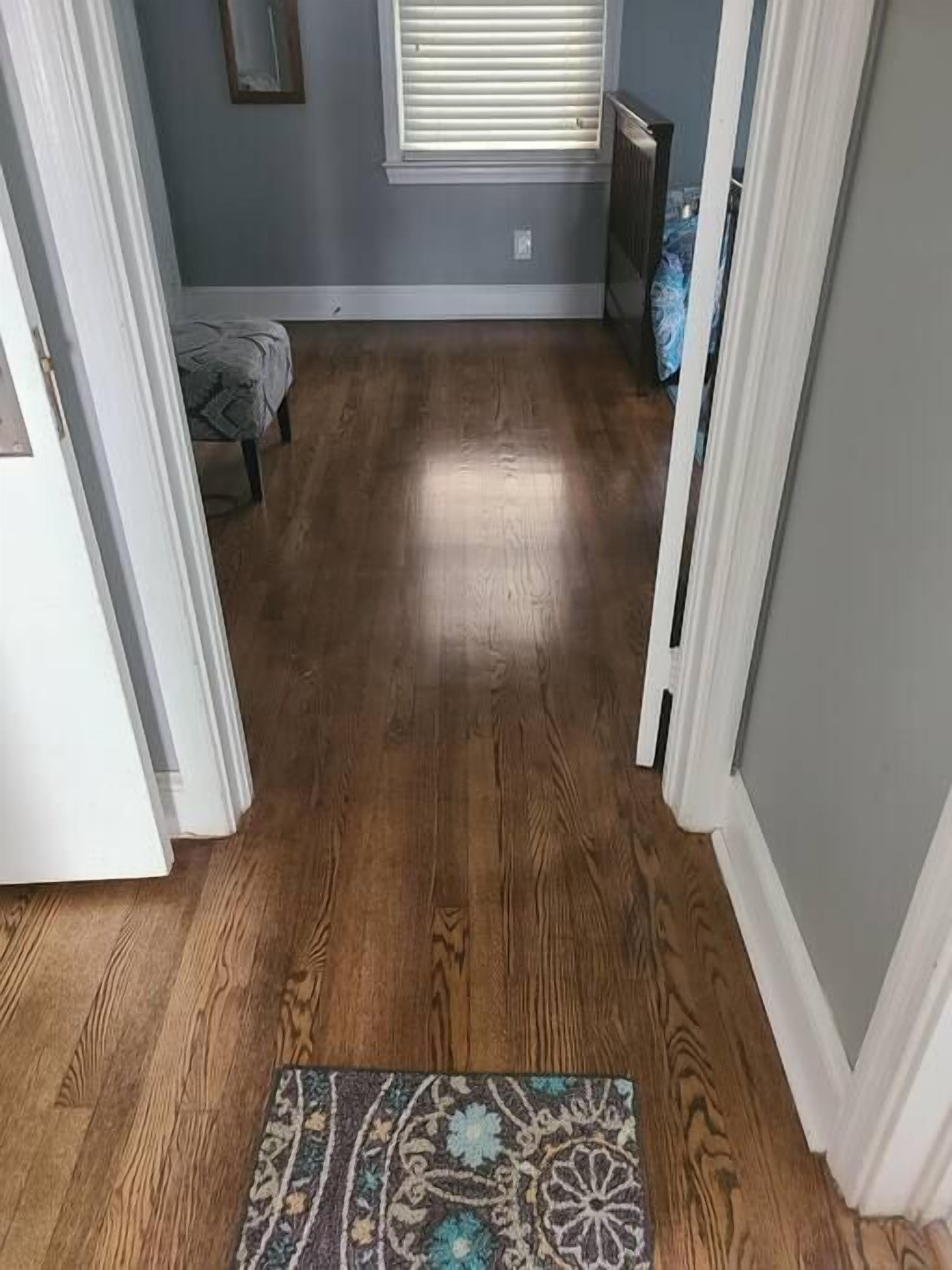 Un couloir doté d’un plancher en bois, d’un tapis à motifs et d’une fenêtre avec des stores.