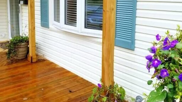 A covered porch with wooden beams, white siding, and blue shutters. - Cozy Ardmore Cottage Main Level (Winston-Salem)
