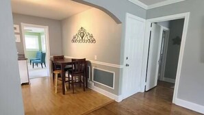 A spacious room with hardwood flooring, a dining area with a table and chairs, and a decorative wall piece. - Cozy Ardmore Cottage Main Level (Winston-Salem)