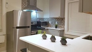 Une cuisine moderne équipée d’un réfrigérateur en acier inoxydable, d’un four à micro-ondes et d’une cuisinière. Trois plantes en pot sont disposées sur le plan de travail central.