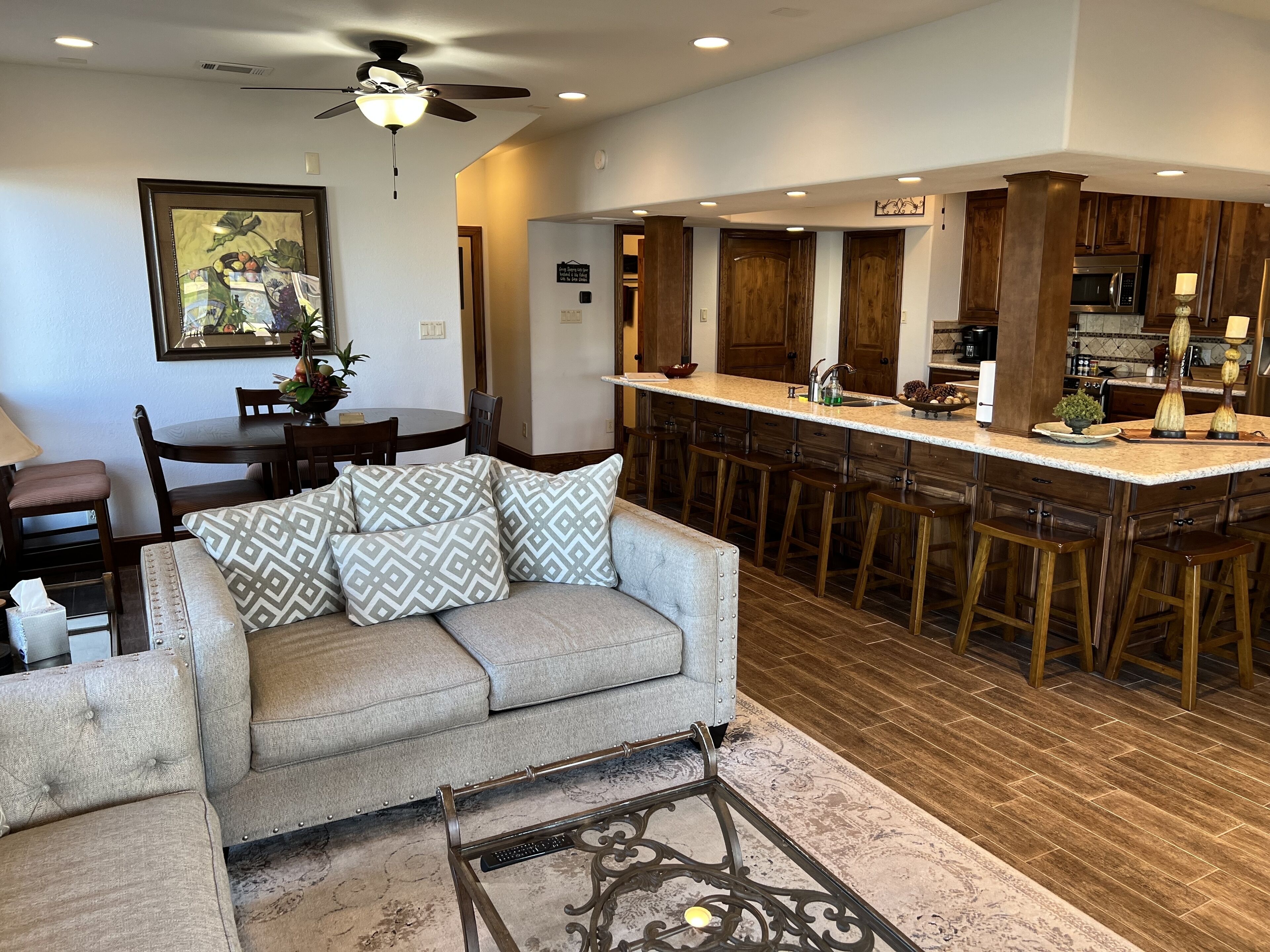 A modern kitchen with wooden cabinets, a bar area, and a dining area with a sofa and chairs.