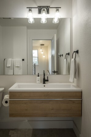 A modern bathroom with a large mirror, white sink, wooden vanity, and three pendant lights.