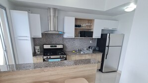 A modern kitchen with white cabinets, a granite countertop, a stove, a sink, and two wooden stools.