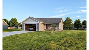 A single-story house with a garage, a well-maintained lawn, and a clear sky. -  HARVEST COTTAGE Cozy home for family memories in a small town.. (Hesston)
