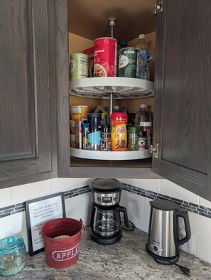 A kitchen with a built-in pantry shelf stocked with various food items and a coffee maker on the countertop. -  HARVEST COTTAGE Cozy home for family memories in a small town.. (Hesston)