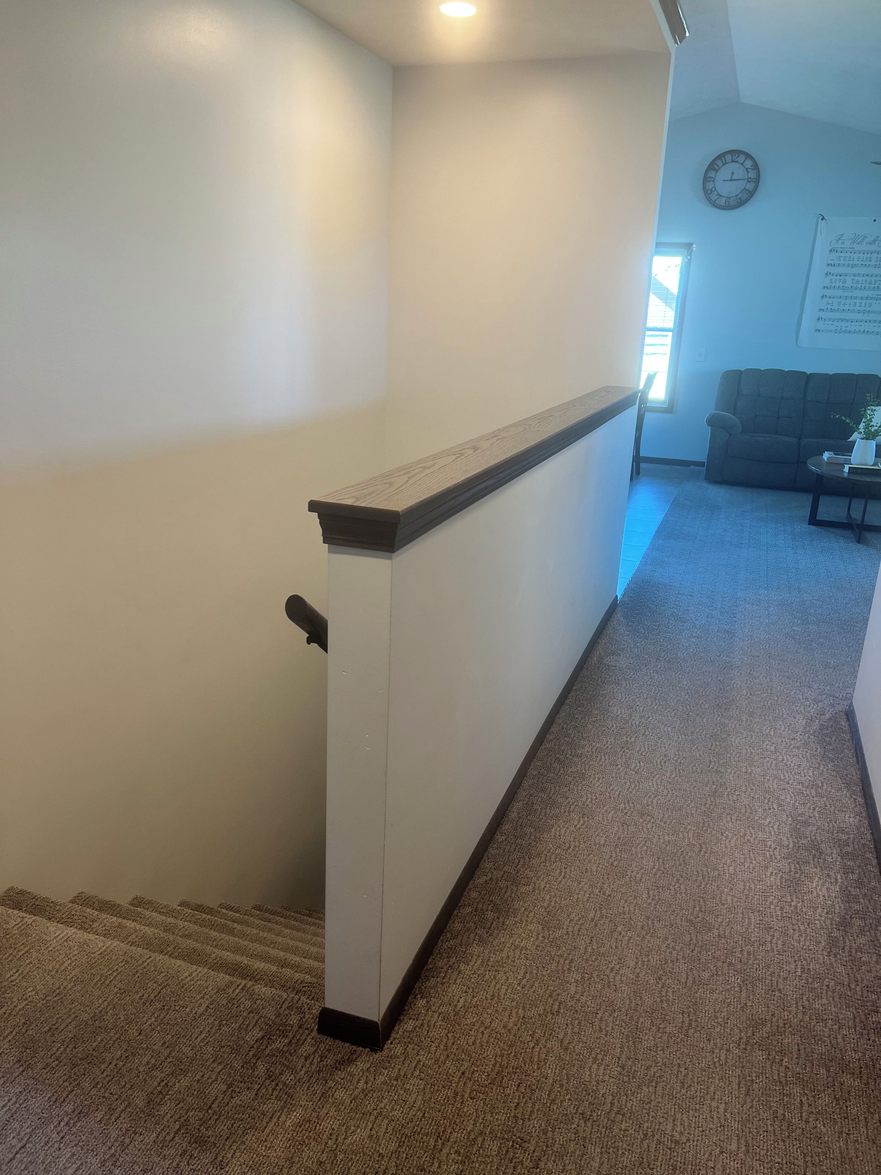 A carpeted hallway with a white radiator, a clock on the wall, and a window allowing natural light.