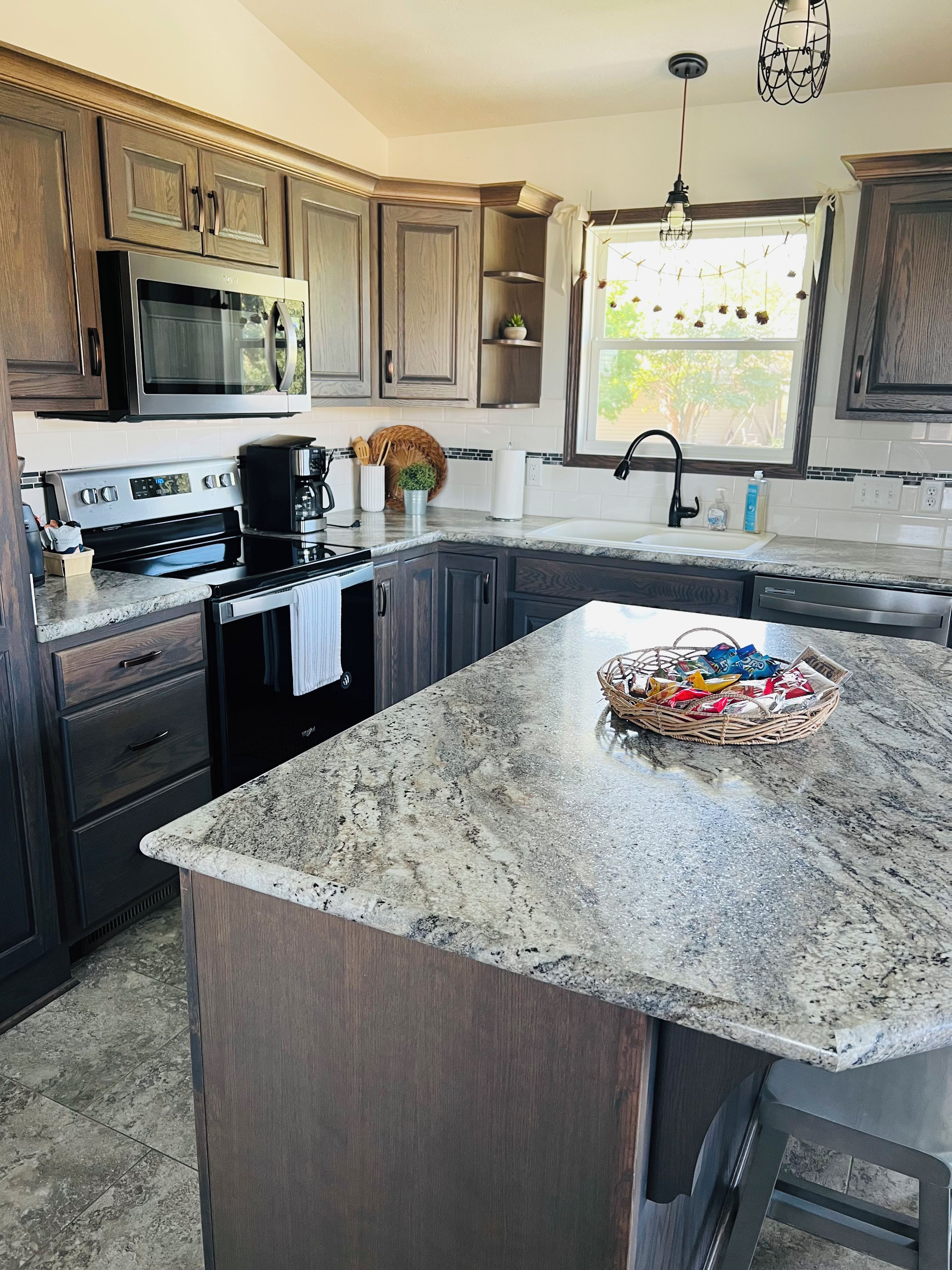 A kitchen with dark wood cabinets, stainless steel appliances, a granite countertop, and a window with a view of greenery.