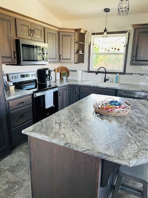 A kitchen with dark wood cabinets, stainless steel appliances, a granite countertop, and a window with a view of greenery. -  HARVEST COTTAGE Cozy home for family memories in a small town.. (Hesston)