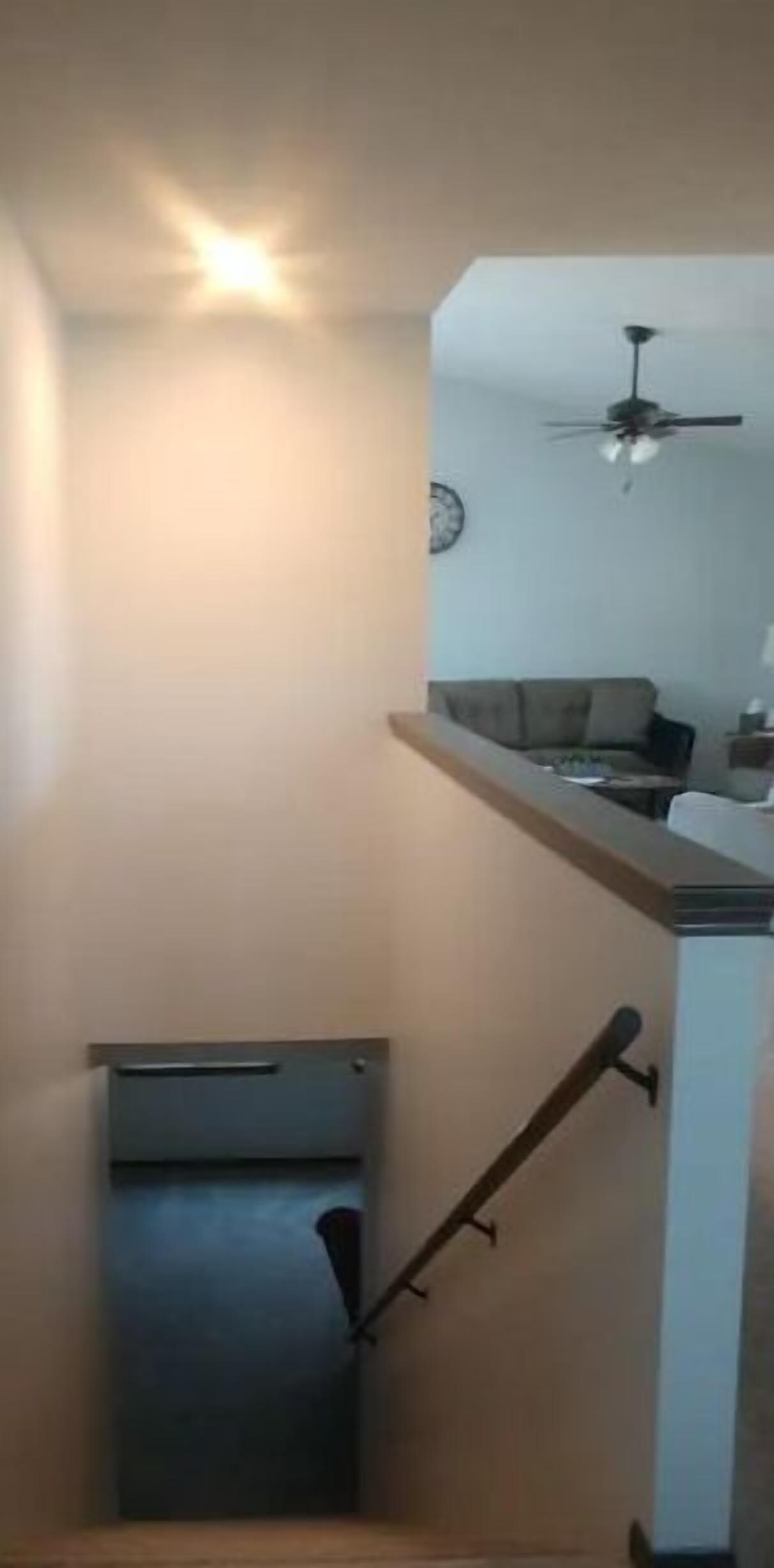 A staircase with a handrail leading to a landing. A ceiling fan is visible in the upper room.