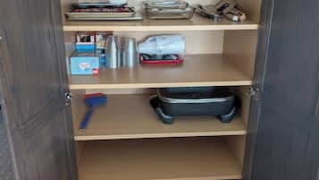 A cabinet with multiple shelves containing kitchenware, a portable stove, and a bag.