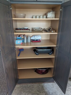 A cabinet with multiple shelves containing kitchenware, a portable stove, and a bag. -  HARVEST COTTAGE Cozy home for family memories in a small town.. (Hesston)