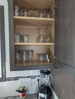 A kitchen with wooden cabinets, a blender on the counter, and various glass containers on shelves. -  HARVEST COTTAGE Cozy home for family memories in a small town.. (Hesston)