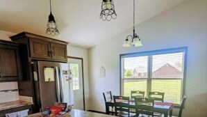 A kitchen with dark wooden cabinets, a granite countertop, and a dining area with a table and chairs. -  HARVEST COTTAGE Cozy home for family memories in a small town.. (Hesston)