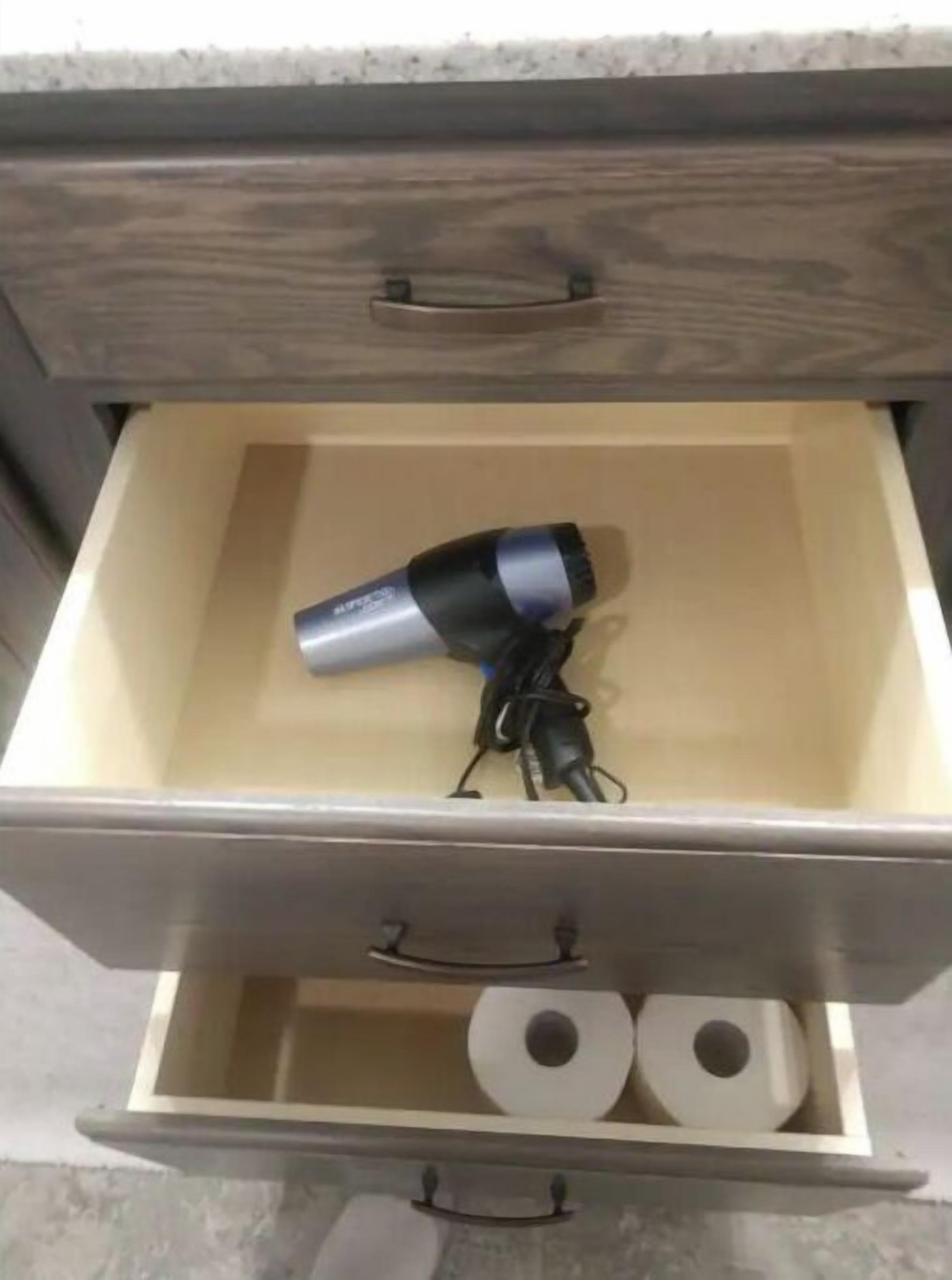 Eine Schublade mit einem Haartrockner und zwei Toilettenpapierrollen.