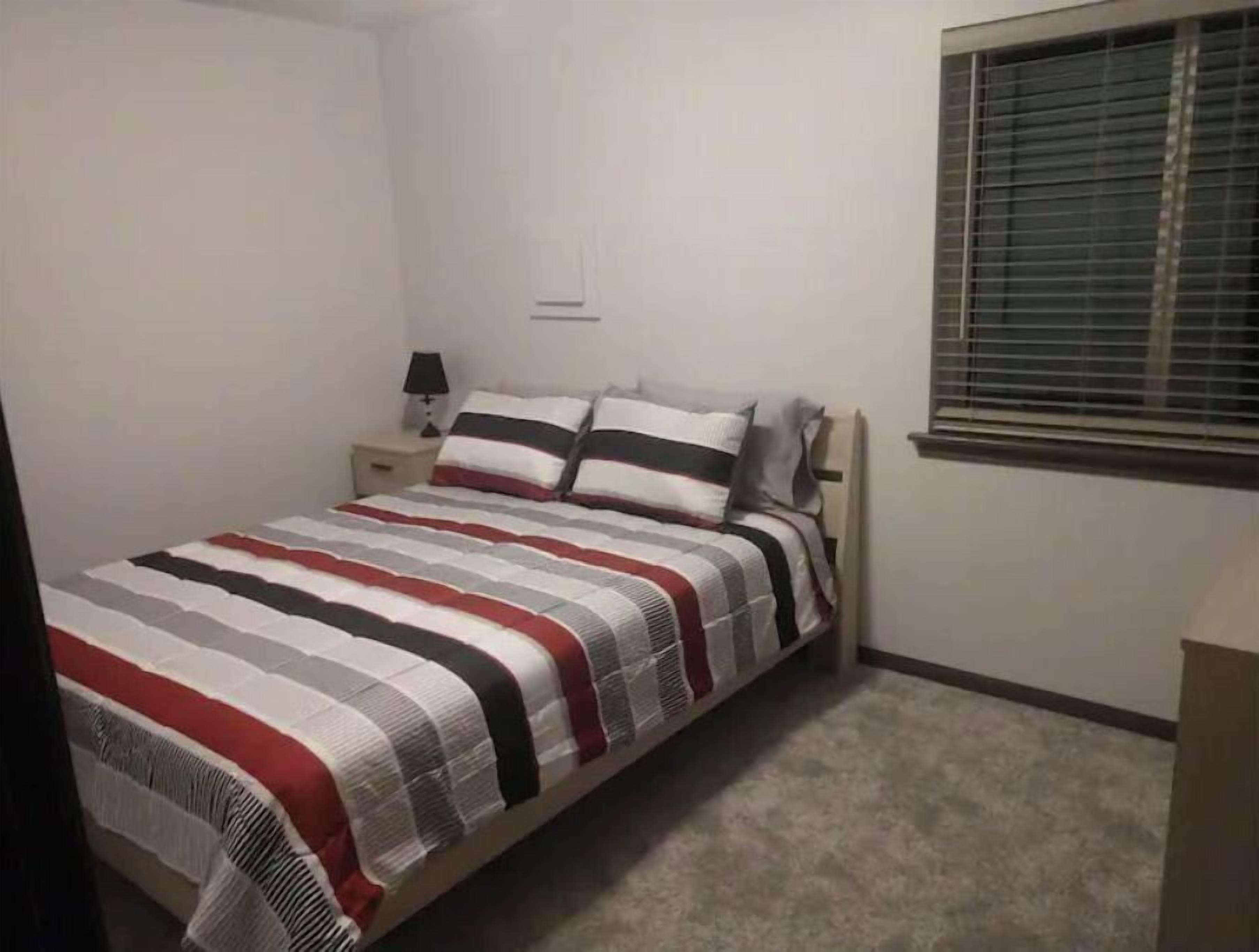 A bedroom with a bed, nightstands, a lamp, and a window with blinds.
