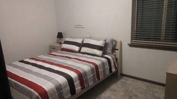 A bedroom with a bed, nightstands, a lamp, and a window with blinds.