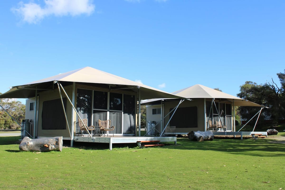 Two mobile homes with large awnings, outdoor seating, and a grassy lawn.