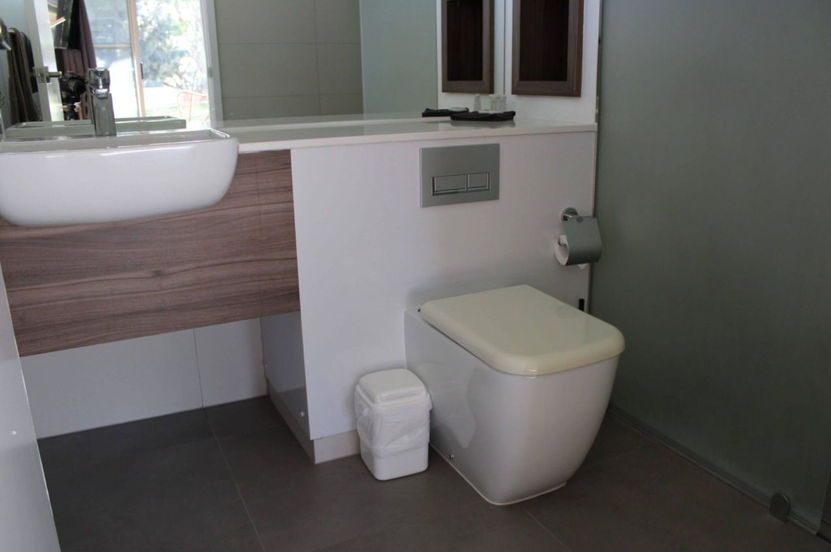 Ein modernes Badezimmer mit einem weißen Waschbecken, einer Toilette und einer kleinen Mülleimer.