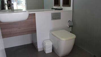 Ein modernes Badezimmer mit einem weißen Waschbecken, einer Toilette und einer kleinen Mülleimer.