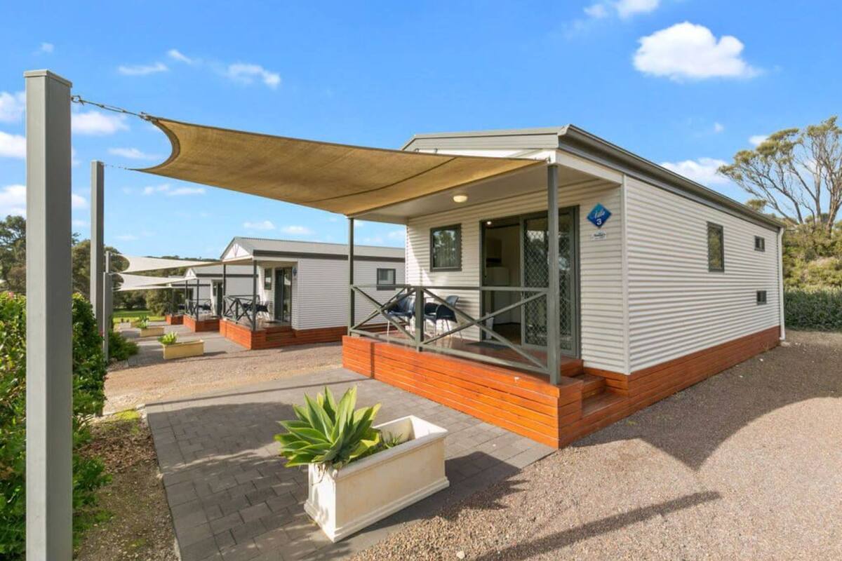 A mobile home with a covered patio, outdoor seating, and a garden area.
