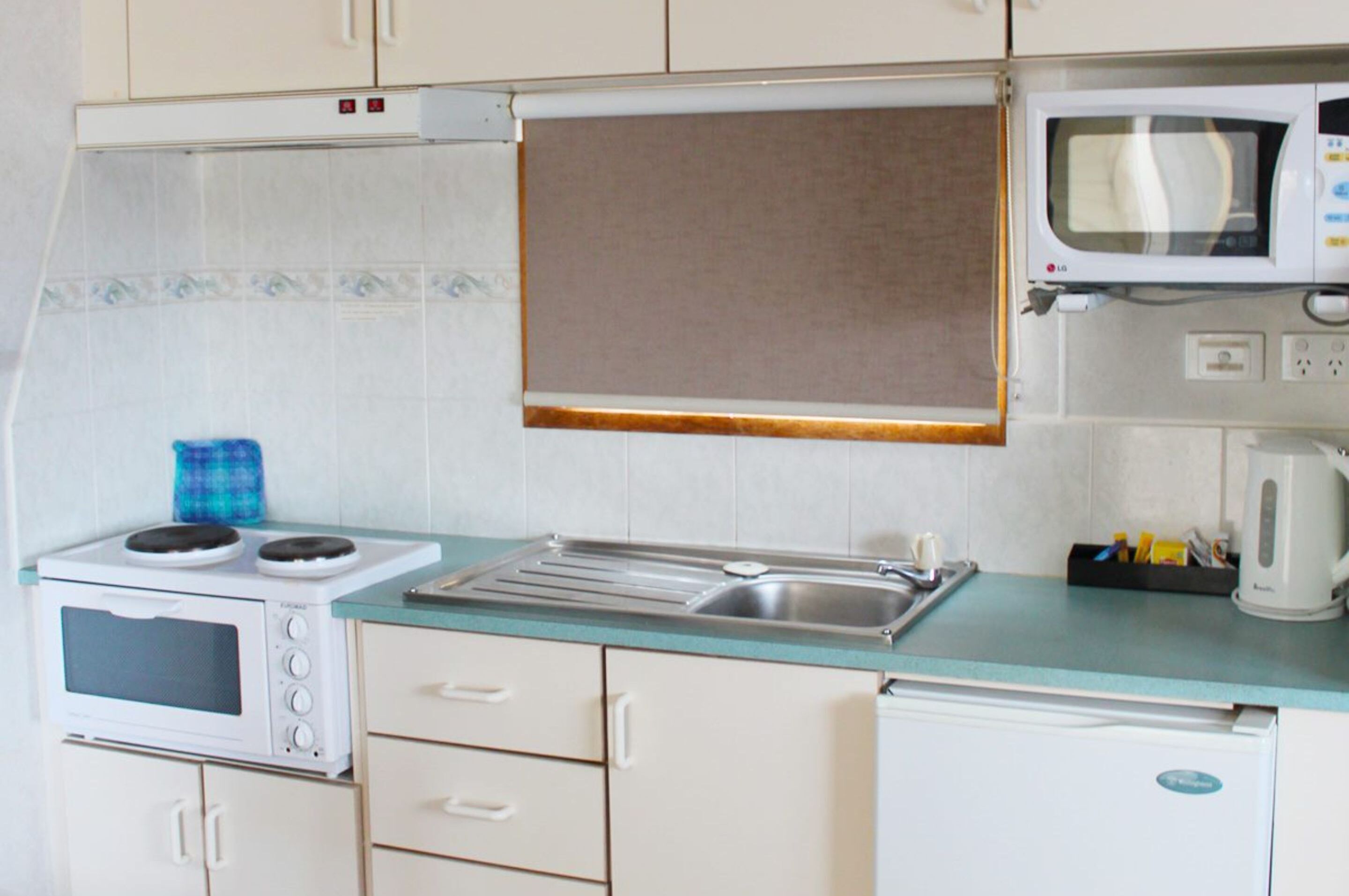 Een kleine keuken met een magnetron, fornuis en wastafel.