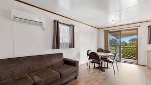 Una sala de estar moderna con un sofá marrón, una mesa de comedor con sillas y un ventanal corredizo que da a un balcón.