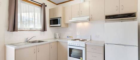 A compact kitchen with a sink, stove, microwave, and refrigerator.